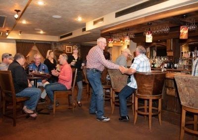 A group of people are sitting at tables and standing at a bar in a restaurant.
