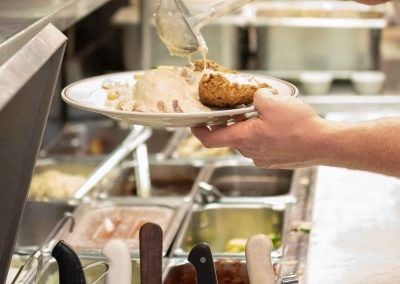 A person is pouring sauce on a plate of food in a kitchen.