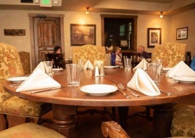 A round table with plates , napkins , glasses and silverware on it in a restaurant.
