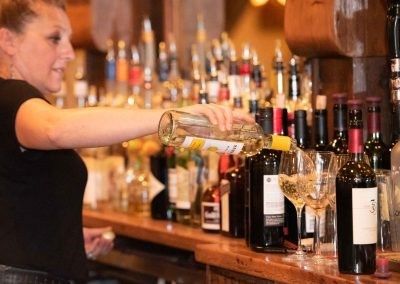 A woman is pouring wine into a glass at a bar.