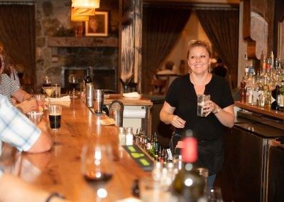 A woman is standing behind a bar holding a glass of wine.