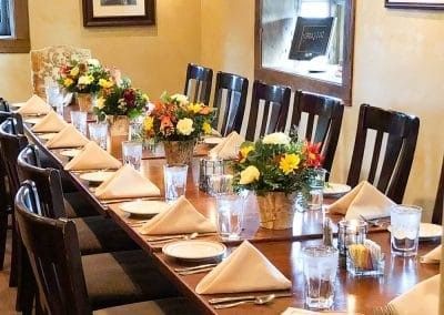 A long table with plates , napkins , glasses and flowers on it.