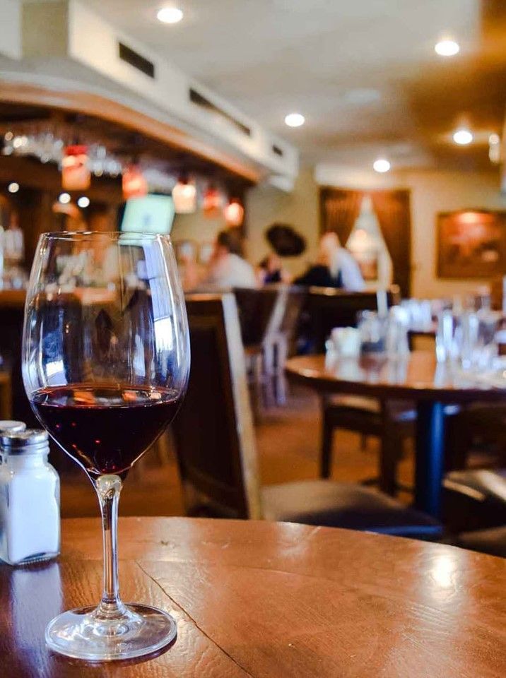 A glass of wine is sitting on a wooden table in a restaurant.