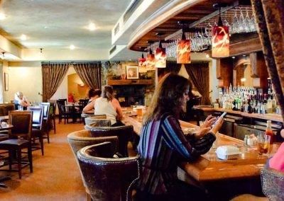 A woman is sitting at a bar in a restaurant looking at her phone.