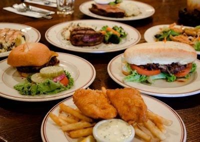 A table topped with plates of food including hamburgers , fish and french fries.