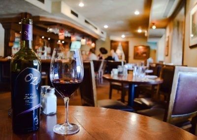 A bottle of wine and a glass of wine are on a table in a restaurant.