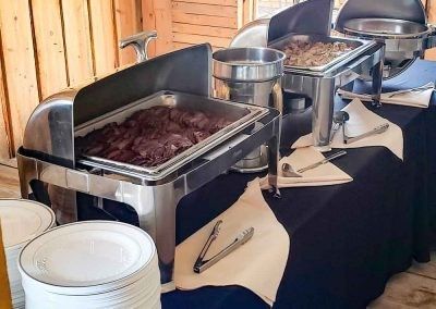 A buffet table with plates , tongs , and trays of food on it.