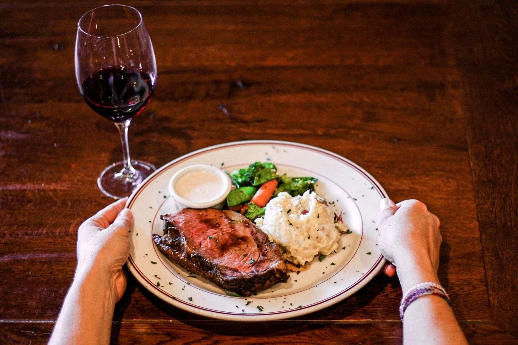 A Person Is Holding a Plate of Food Next to A Glass of Wine.