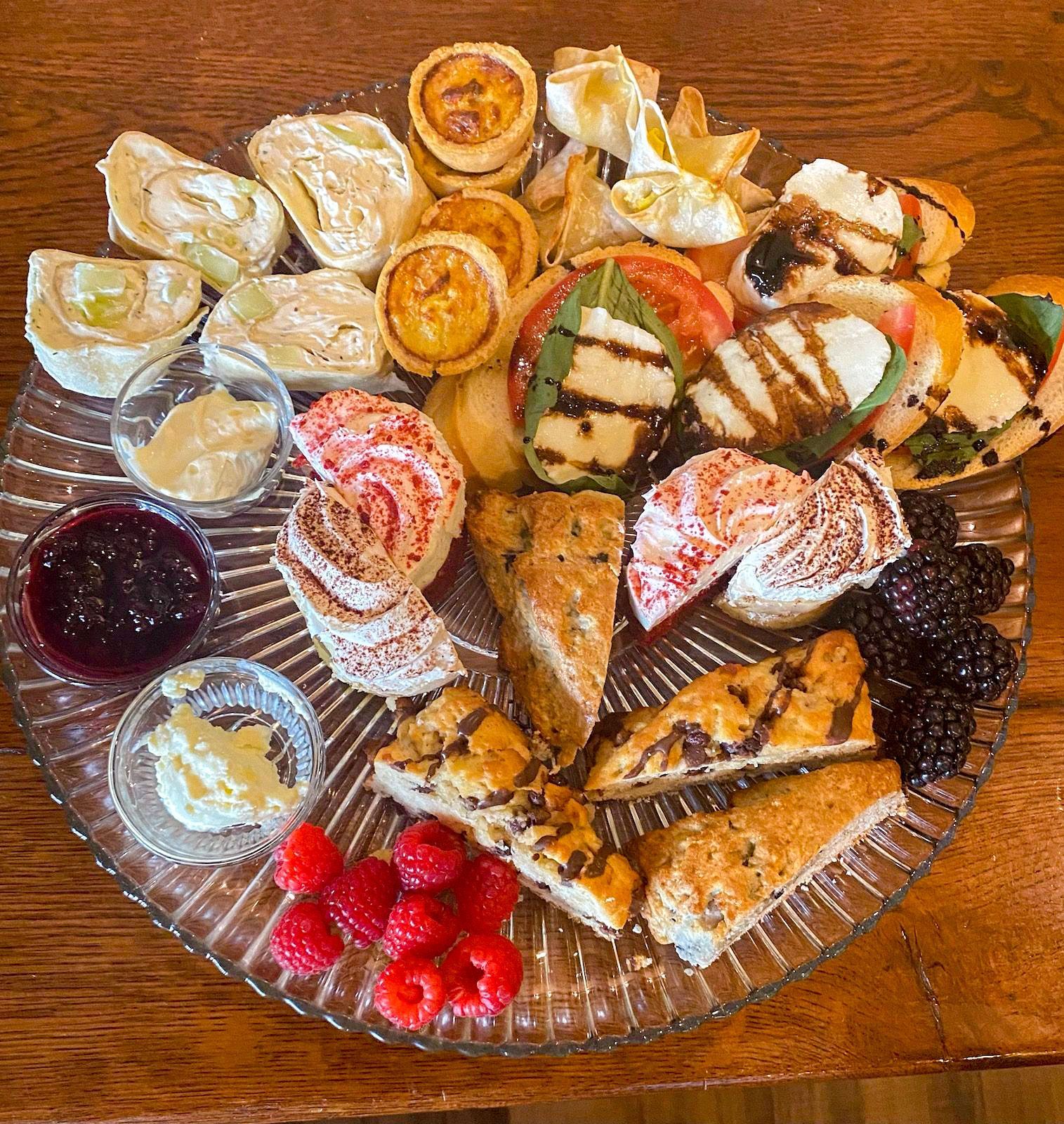 A glass plate topped with a variety of pastries and fruit on a wooden table.