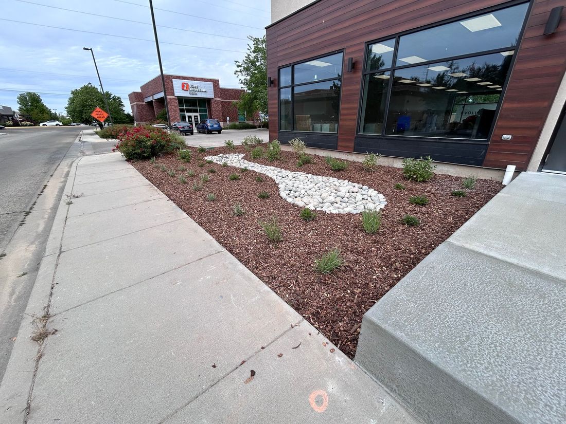Sidewalk beside a brick storefront with a landscaped bed of red mulch and white rocks along the curb.