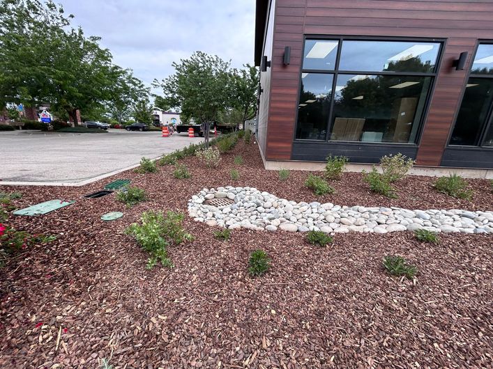 Landscaped mulch bed with white stones beside a brick building and parking lot