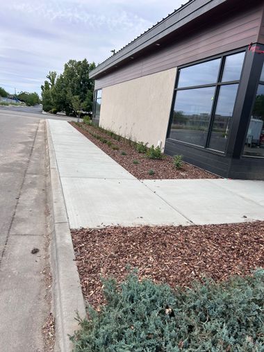 Sidewalk beside a beige building with dark windows and red gravel landscaping.
