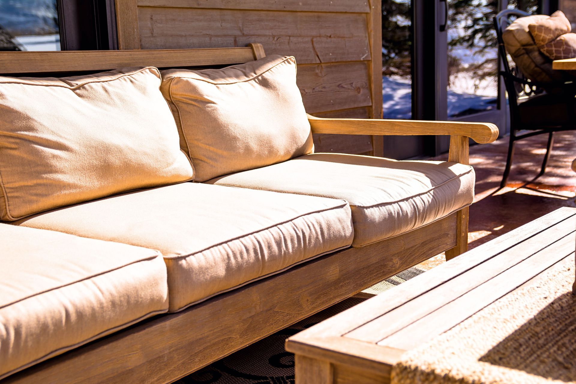 Wooden outdoor sofa with beige cushions on a sunlit deck beside a table