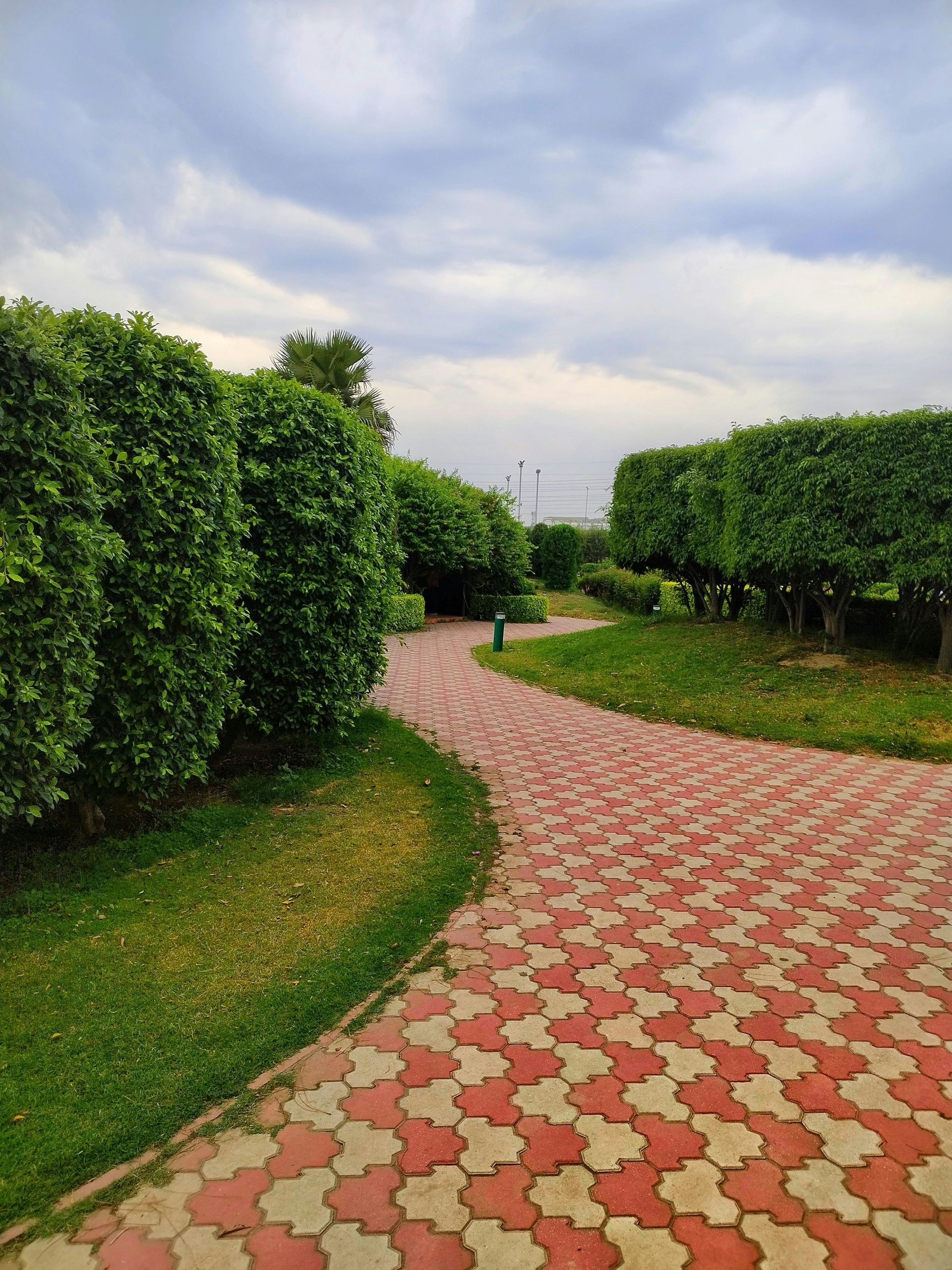 Curving red-and-cream tiled path through green trees under a cloudy sky