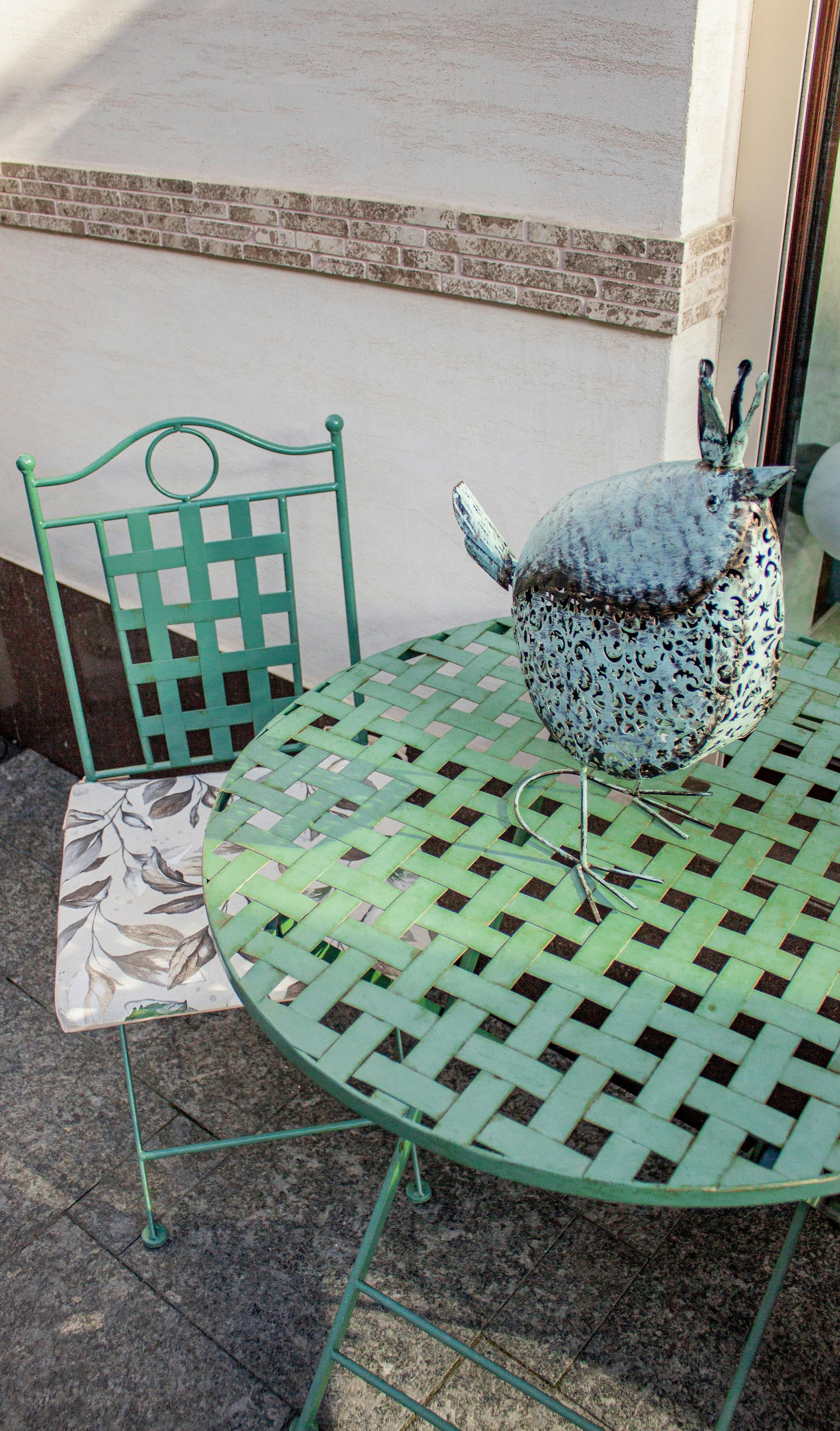 Mint-green metal patio table and chair with a spotted blue pot on the table against a wall.