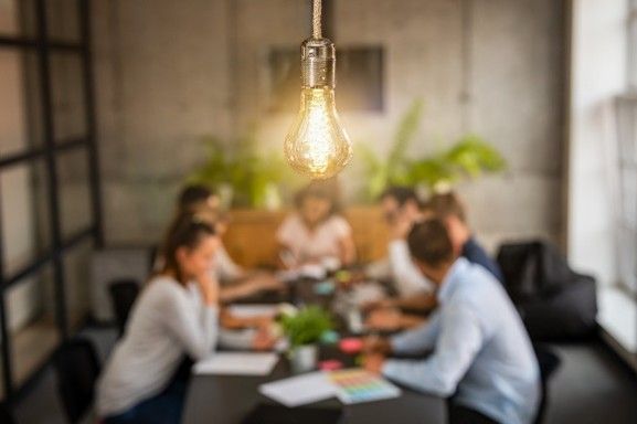 A group of people are sitting around a table in a conference room. There is a bright lightbulb in front.