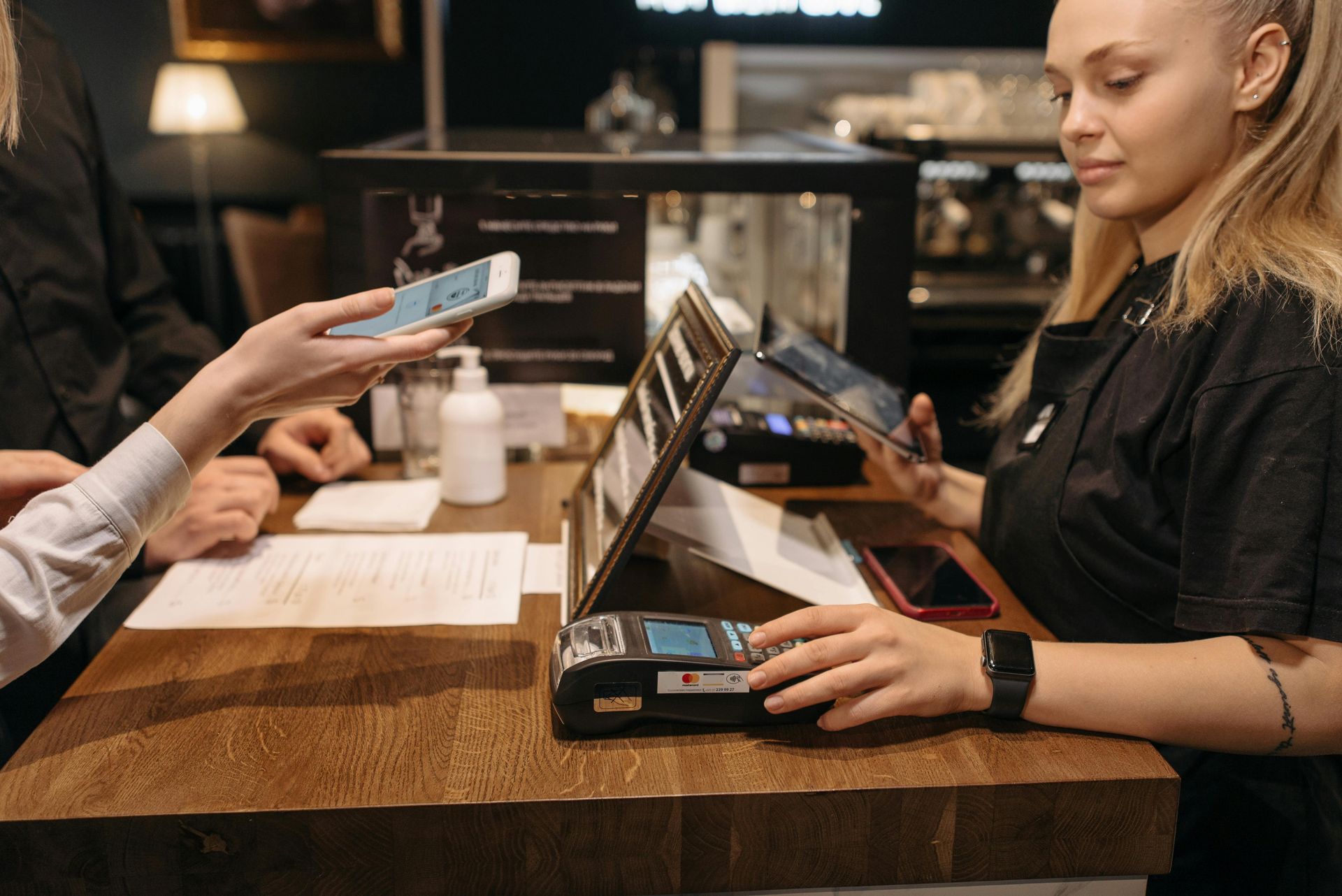 A woman is sitting at a counter in a restaurant holding a cell phone.