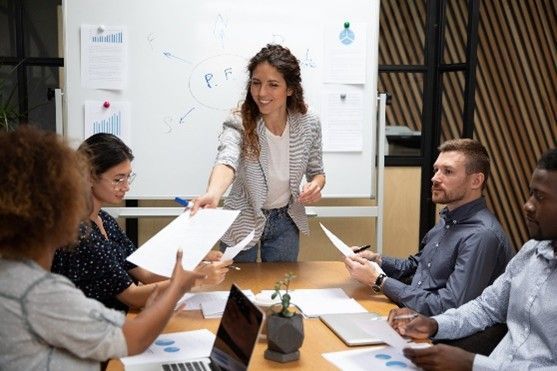 A woman is giving a presentation to a group of people sitting around a table.