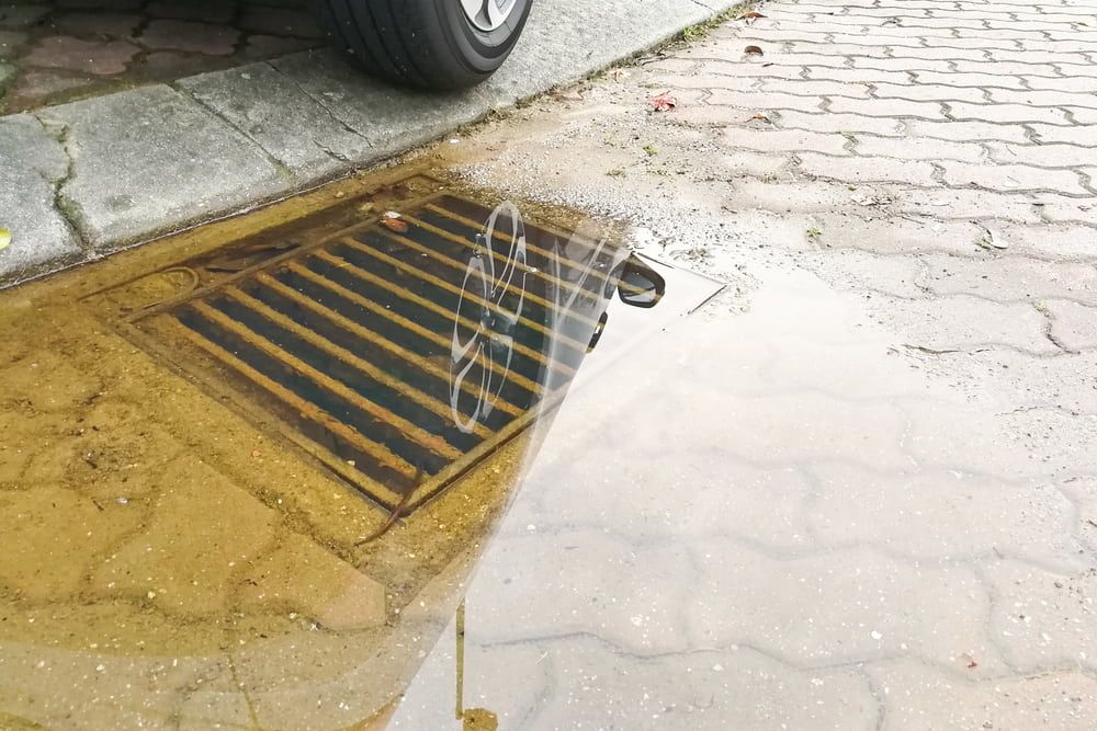 A Car Is Parked On A Brick Sidewalk Next To A Puddle Of Water — Nudges Plumbing In Dubbo, NSW