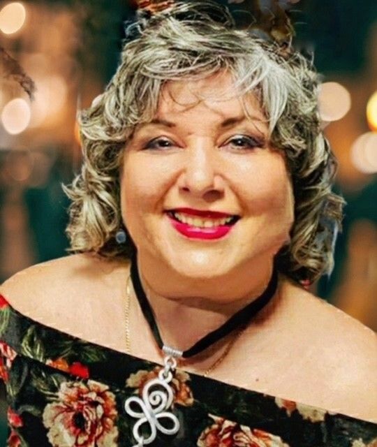 A woman wearing a floral top and a necklace is smiling for the camera.