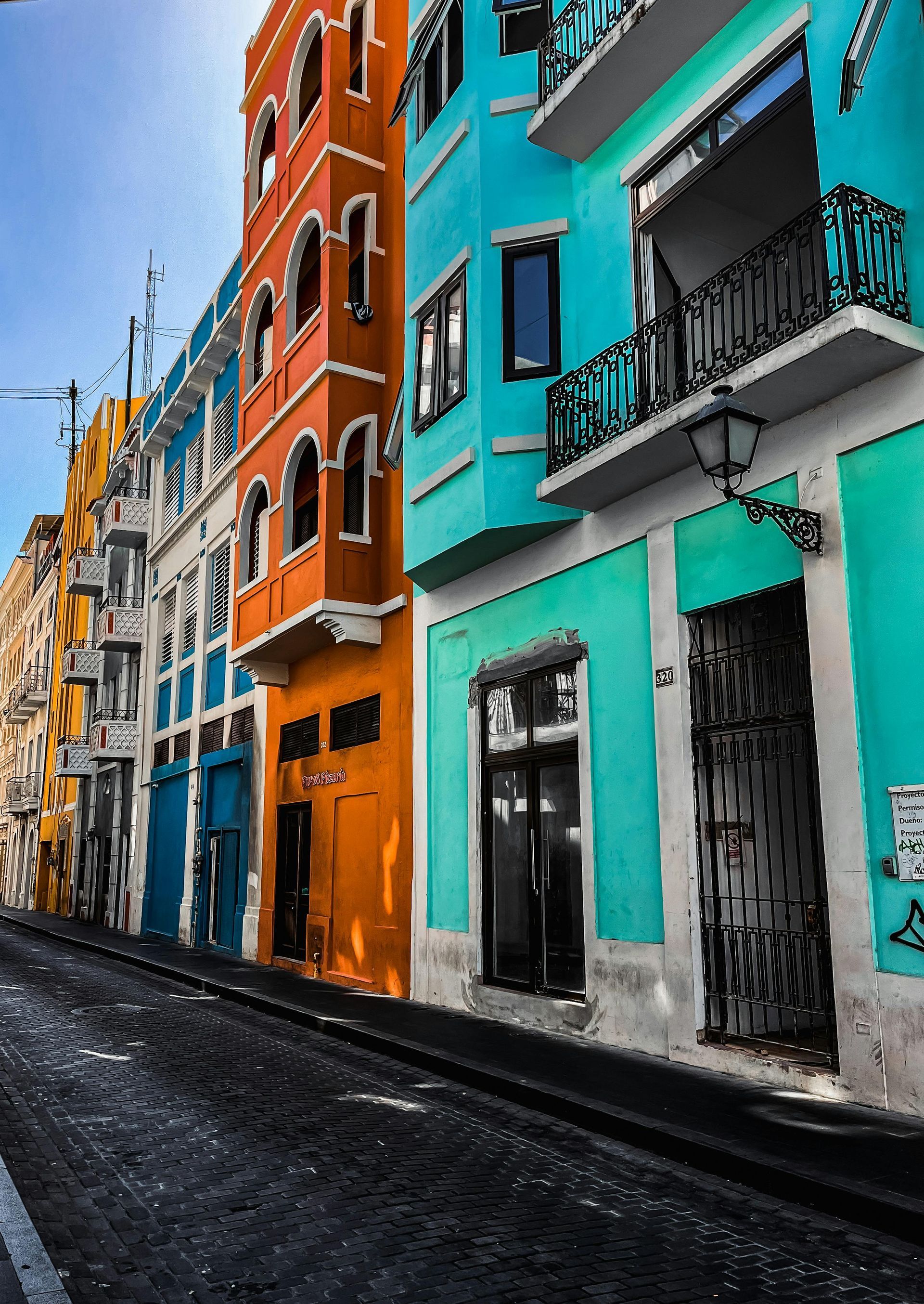 A street lined with colorful, tall buildings in orange, teal, and yellow, featuring wrought iron balconies and details.