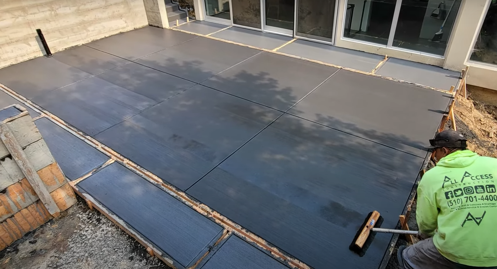 Concrete worker using a broom to add traction to a newly poured concrete patio