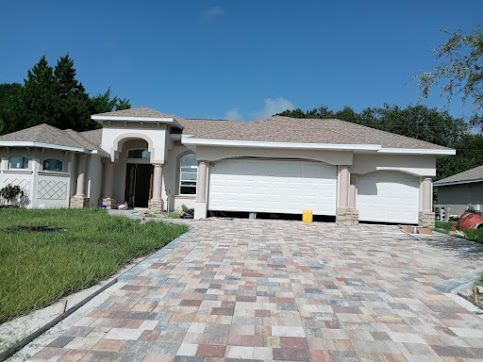 House with a colorful brick driveway, garage doors, and stucco exterior on a sunny day.