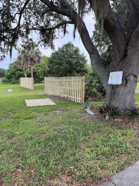 Wooden fence surrounding grassy area next to a large tree; overcast day.