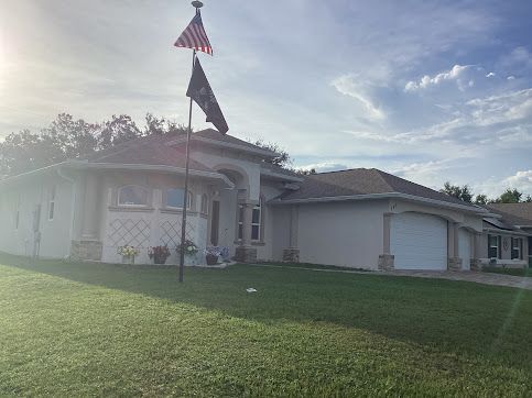 House with American and POW flags on a sunny day; green lawn and blue sky.