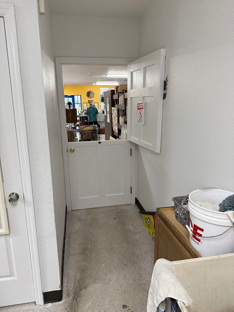 Narrow hallway with a half-open white door leading to a shop. A person is visible inside.