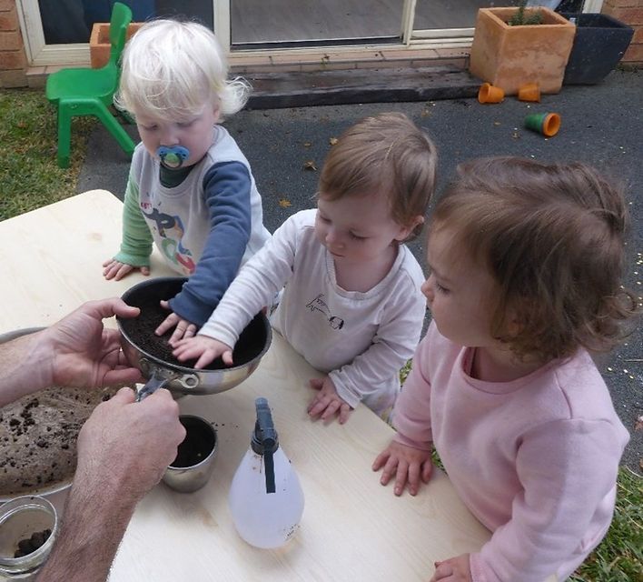 Three children are sitting at a table playing with pots and pans
