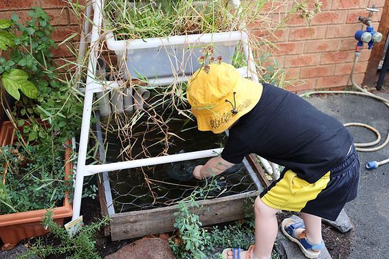 A young boy wearing a yellow hat is working in a garden.