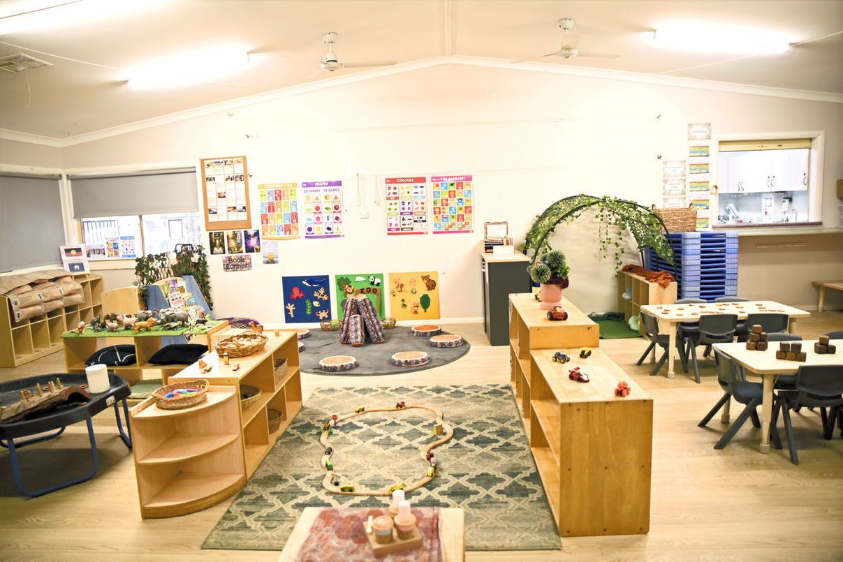 A classroom with tables , chairs , shelves and a rug.