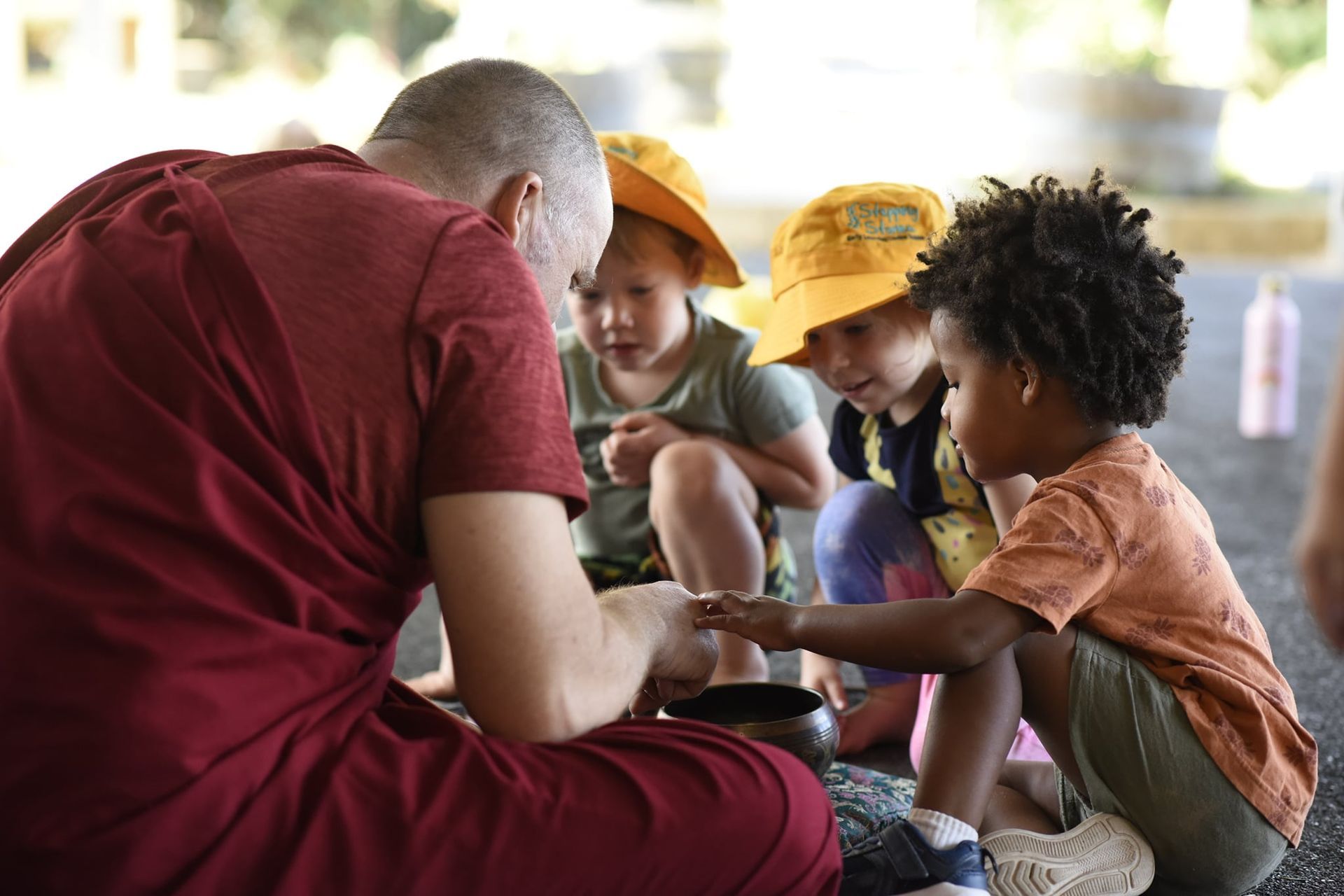 A group of children are sitting around a man in a red robe.