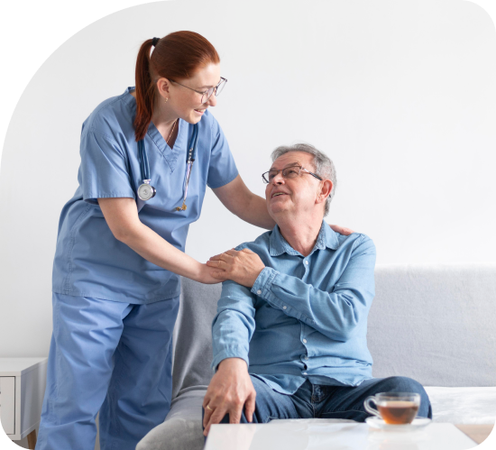 A nurse is helping an elderly man sit on a couch.
