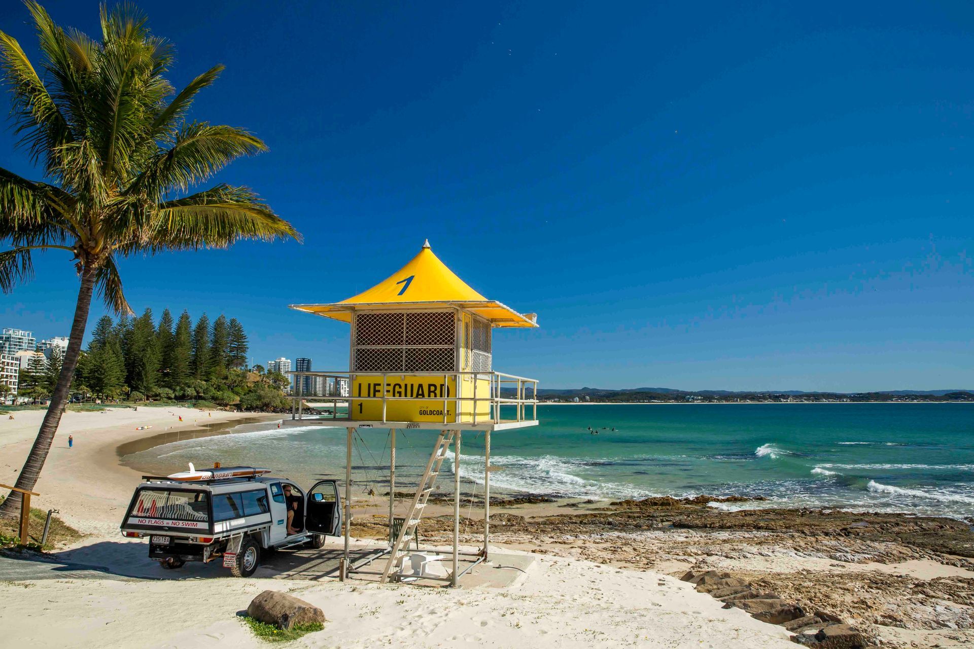 A Yellow Lifeguard Tower On A Beach Next To A Palm Tree — Tweed Byron Recycling In Tweed Heads, NSW