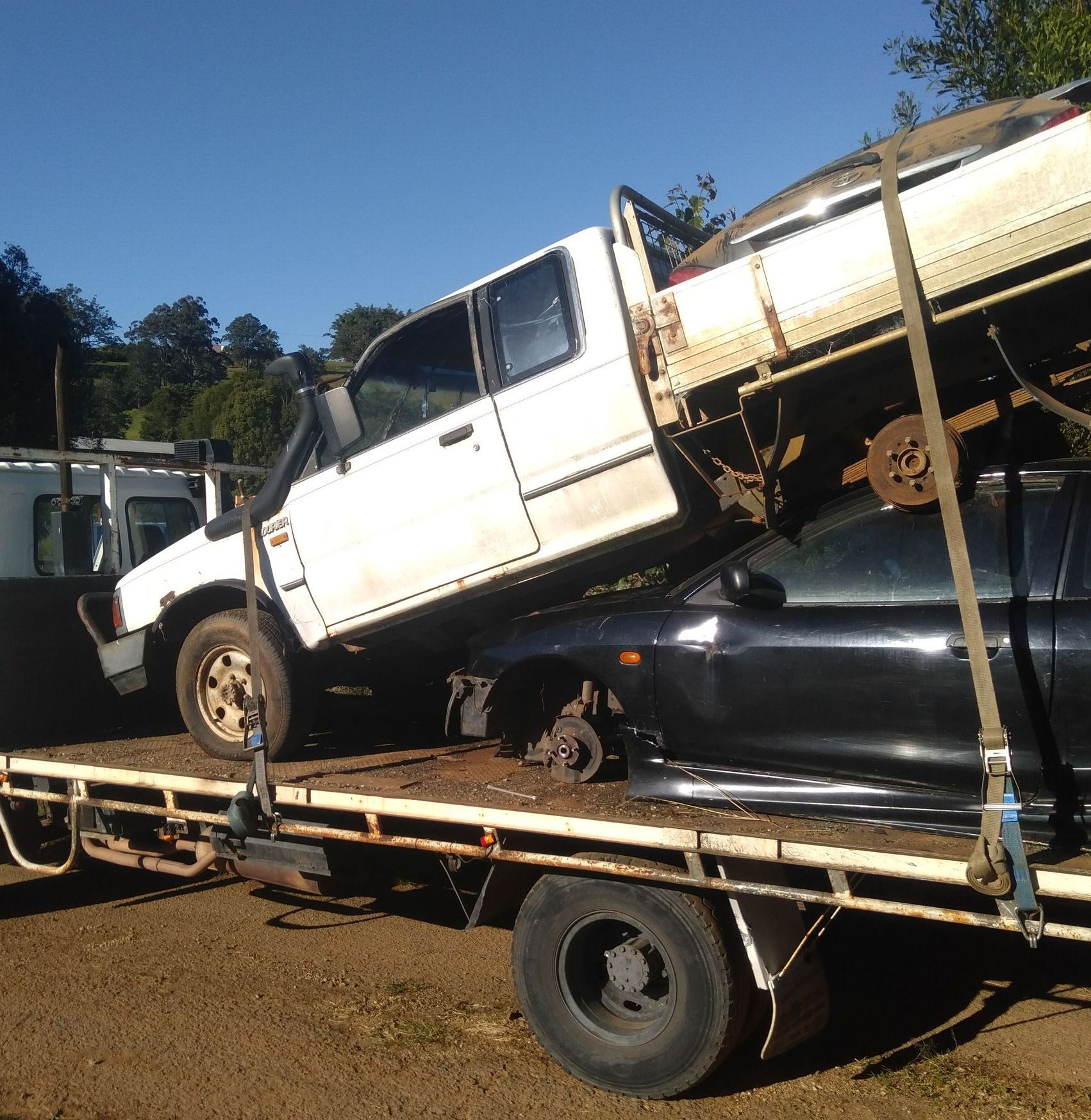 A White Truck Is Sitting On Top Of A Black Car On A Flatbed Truck — Tweed Byron Recycling In Tweed Heads, NSW