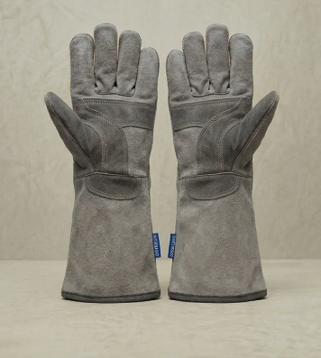 Un par de guantes de trabajo grises colocados en posición vertical sobre una superficie lisa sobre un fondo beige.