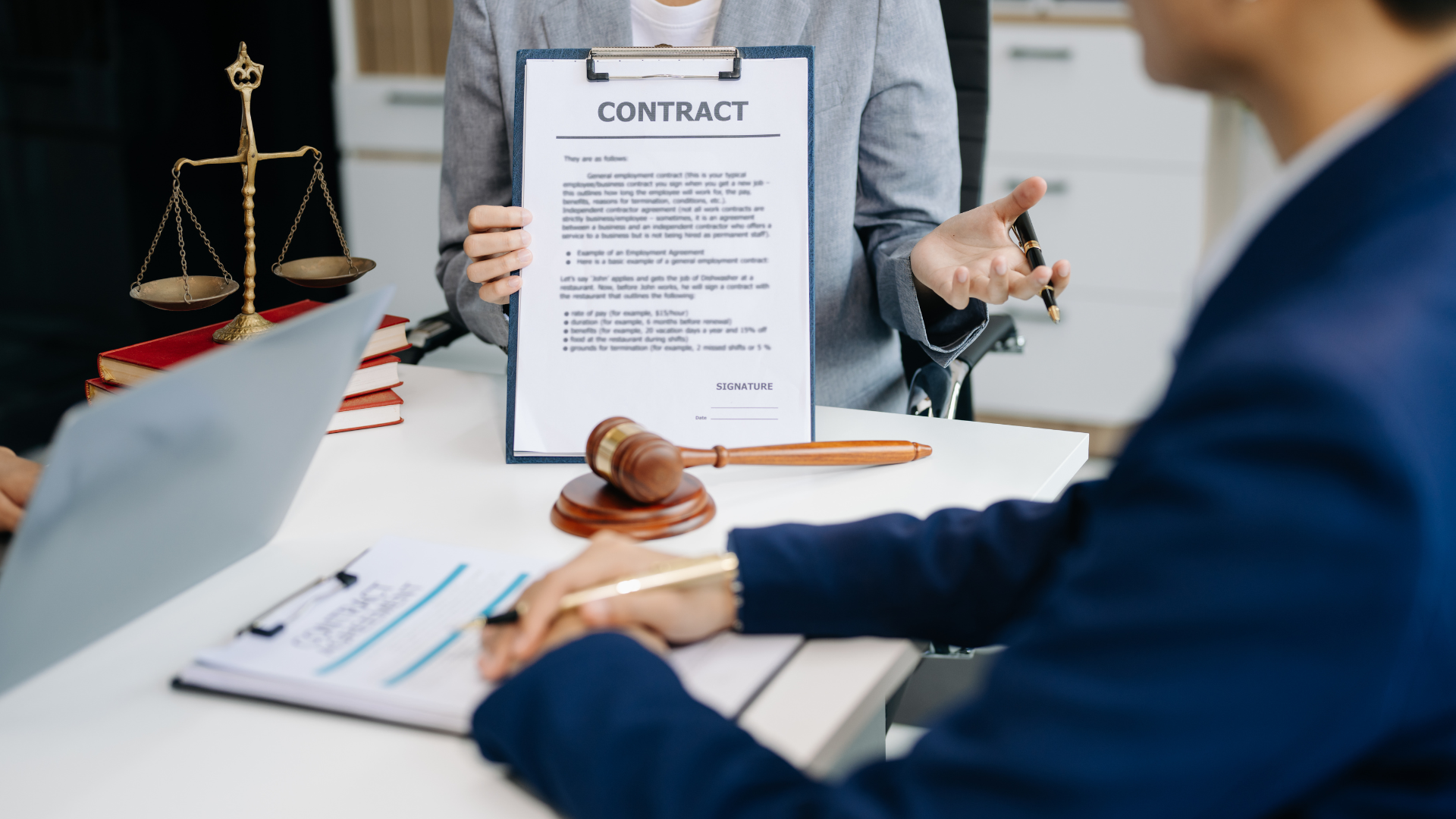 People shaking hands at a desk with a gavel, scales of justice, and a laptop.