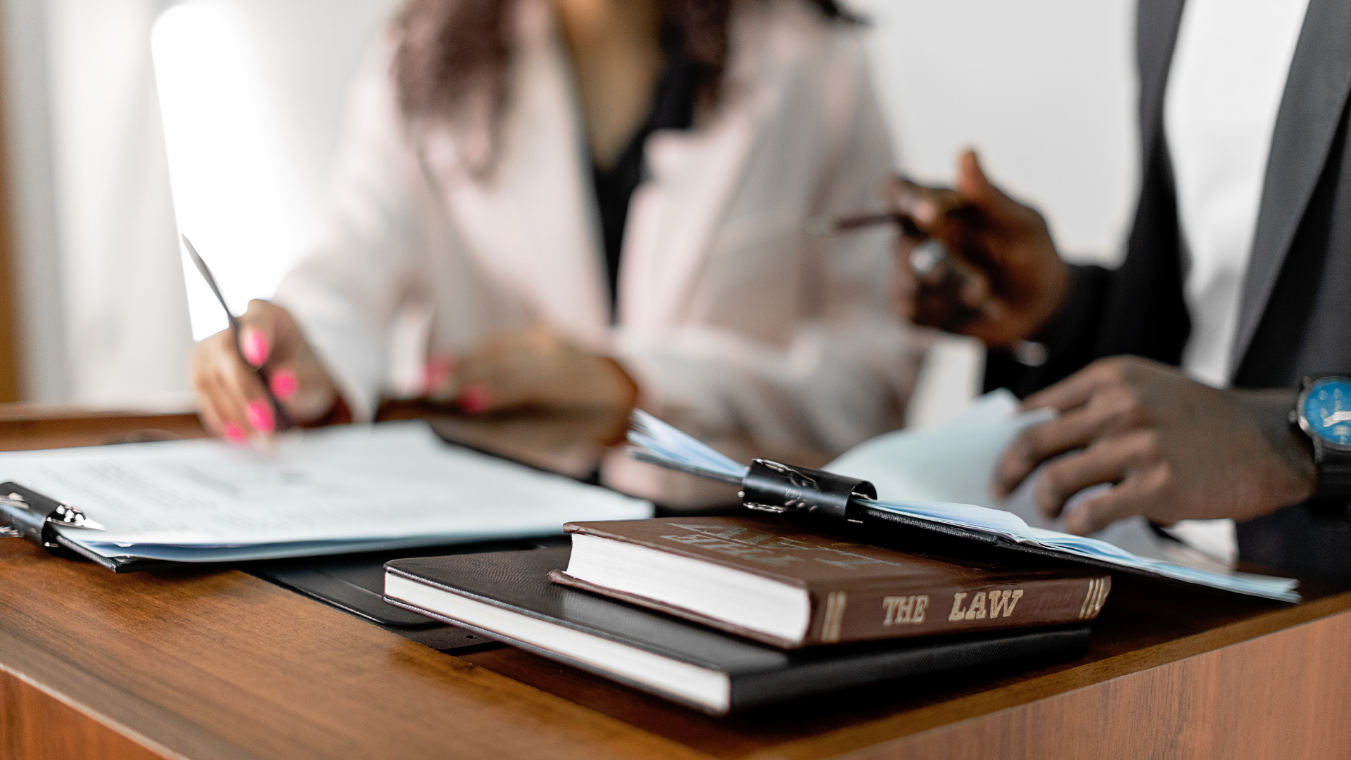 Lawyer gesturing, client writing; books, gavel, and scales of justice on desk.
