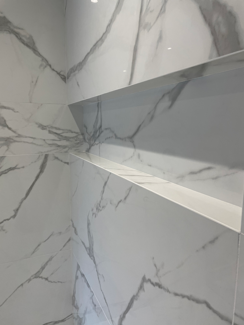 Une salle de bain avec un mur en marbre et une étagère dans la douche.