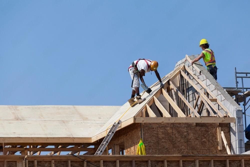 Two construction workers are working on the roof of a building under construction.