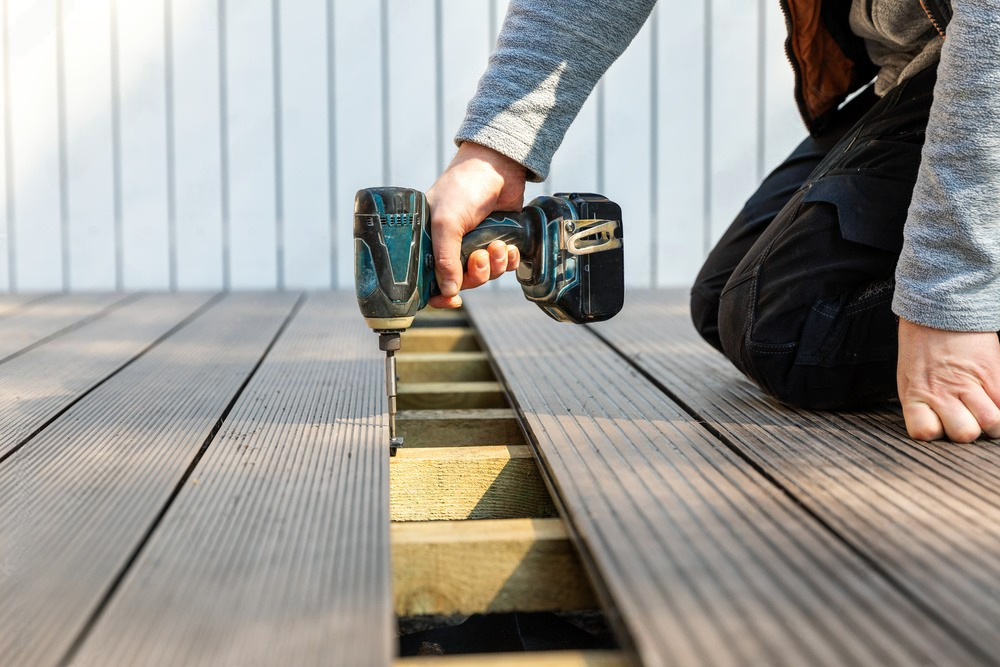 A man is installing a wooden deck with a drill.