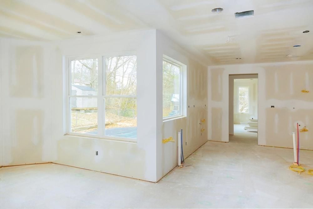 An empty room with drywall and windows in a house under construction.