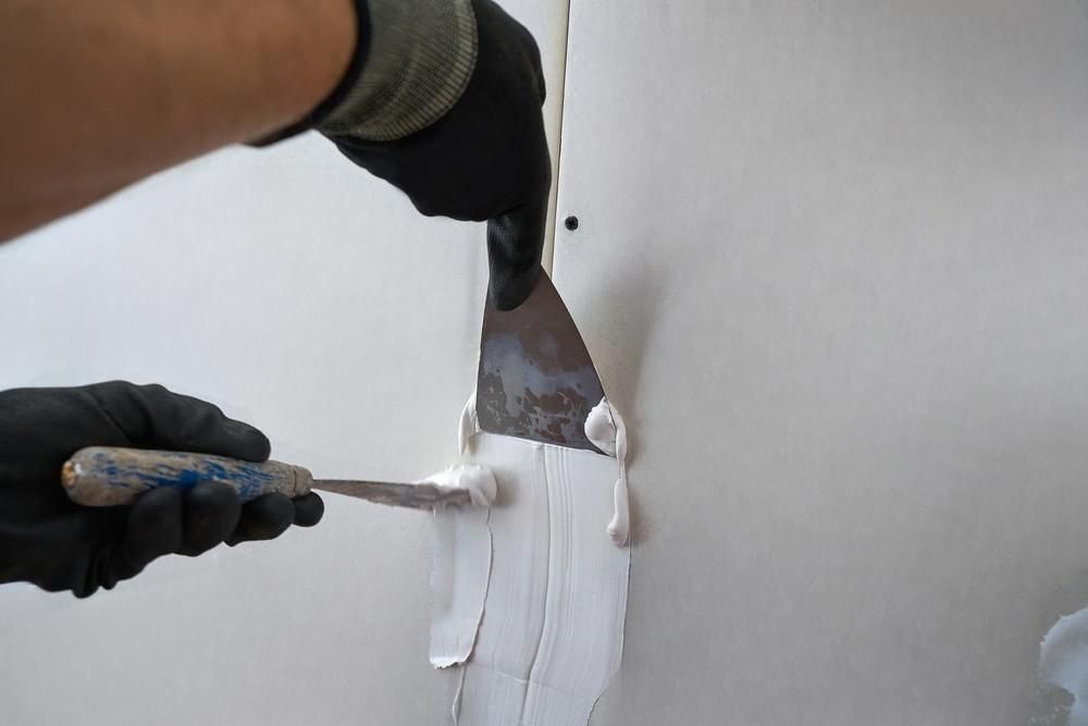 A person is holding a spatula and applying plaster to a wall.