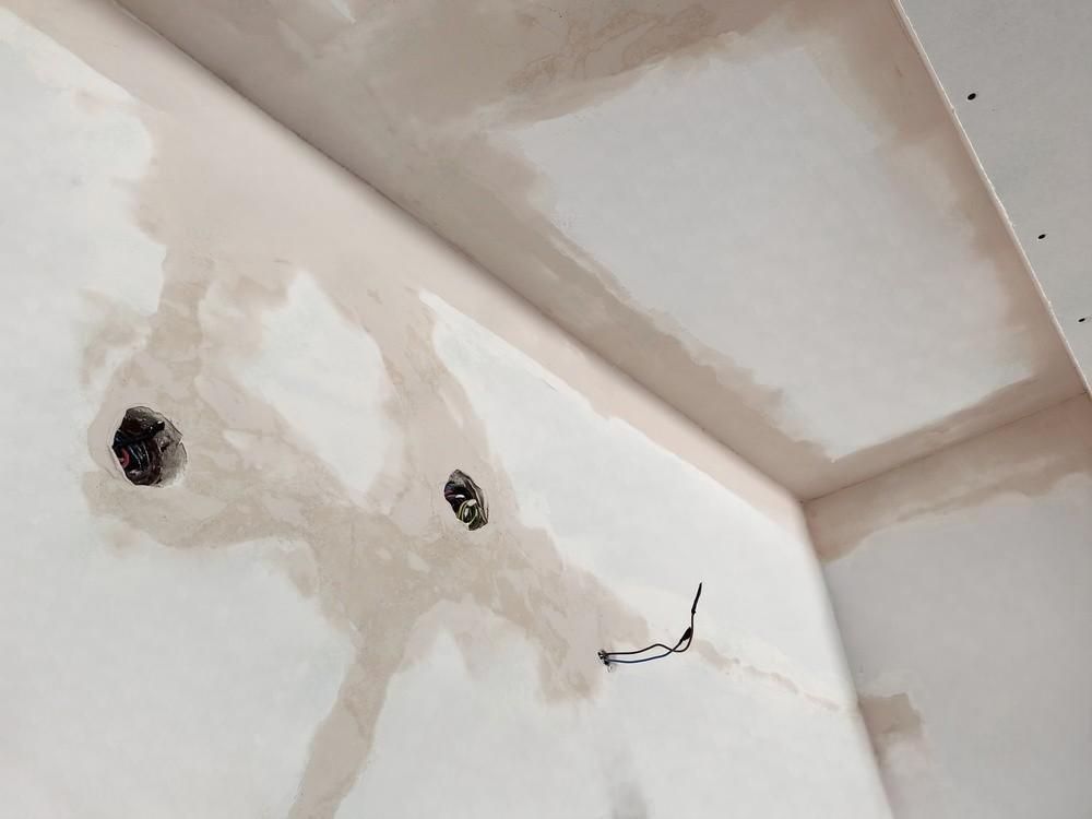 A corner of a room with a hole in the wall and a hole in the ceiling.