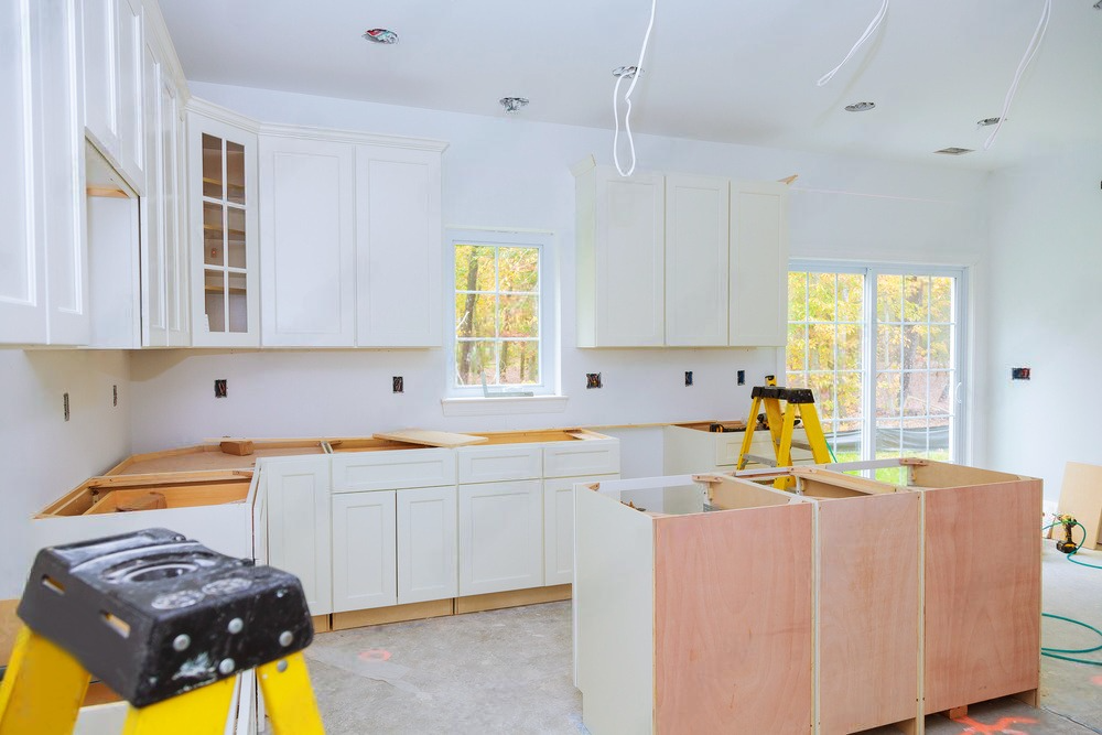 A kitchen under construction with white cabinets and a yellow ladder.