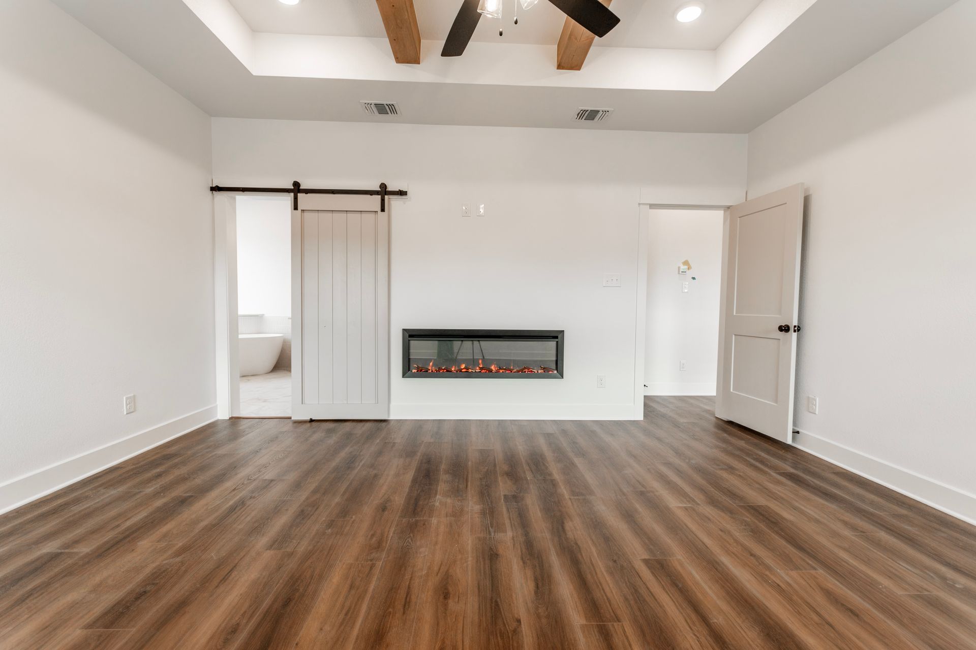 Spacious bedroom with wood floors, fireplace, and sliding barn door leading to bathroom.