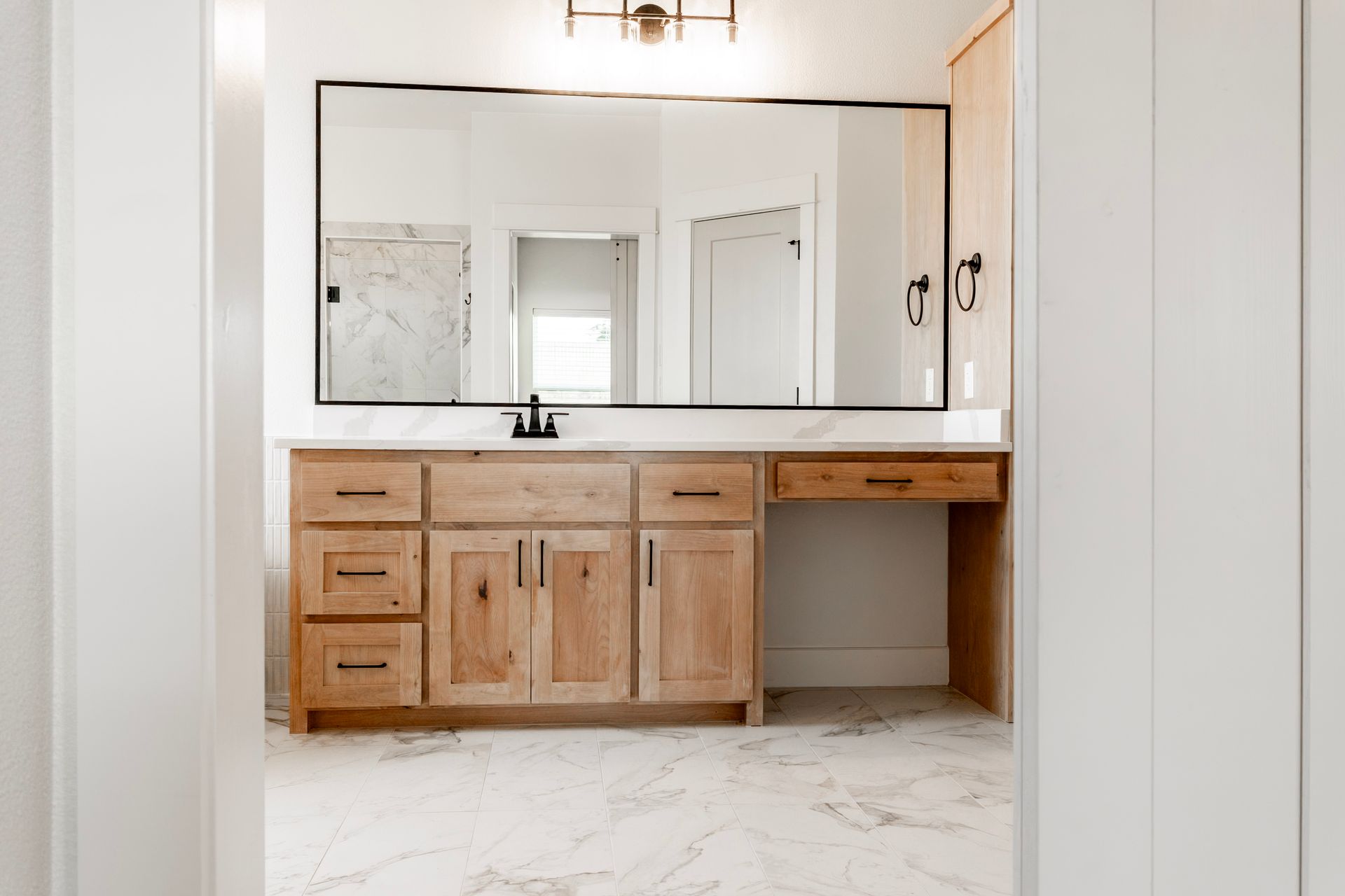 Bathroom with a large mirror above a light wood vanity and marble flooring.
