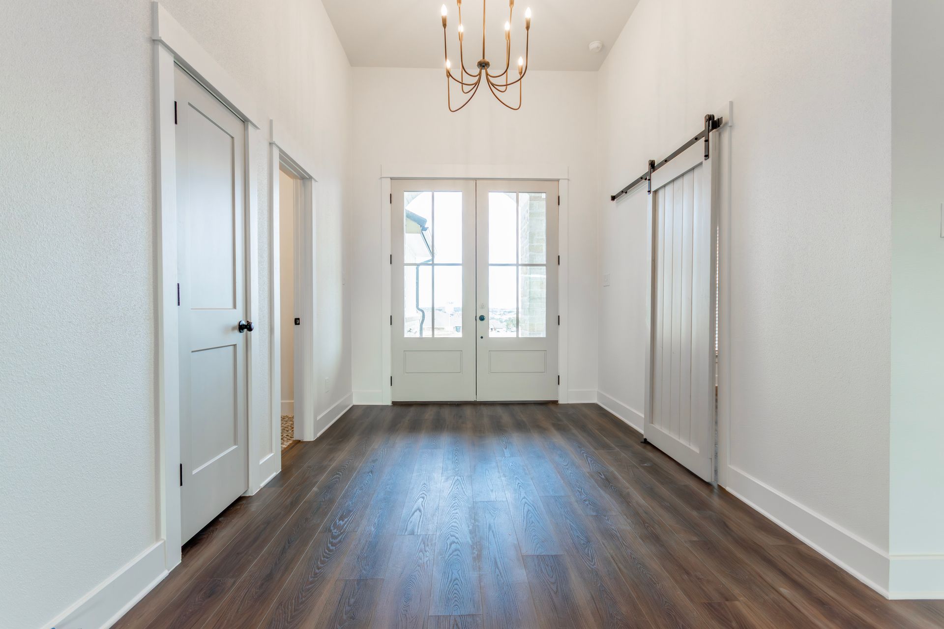 Entryway with dark wood floor, white walls, and a chandelier. French doors lead outside, a sliding door is on the right, and a door on the left.